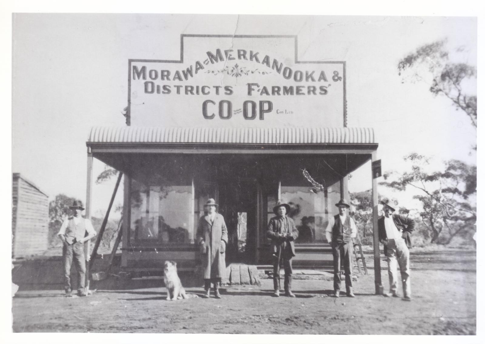 B/W photograph of 5 men and a dog standing in front of a rural shop in 1917