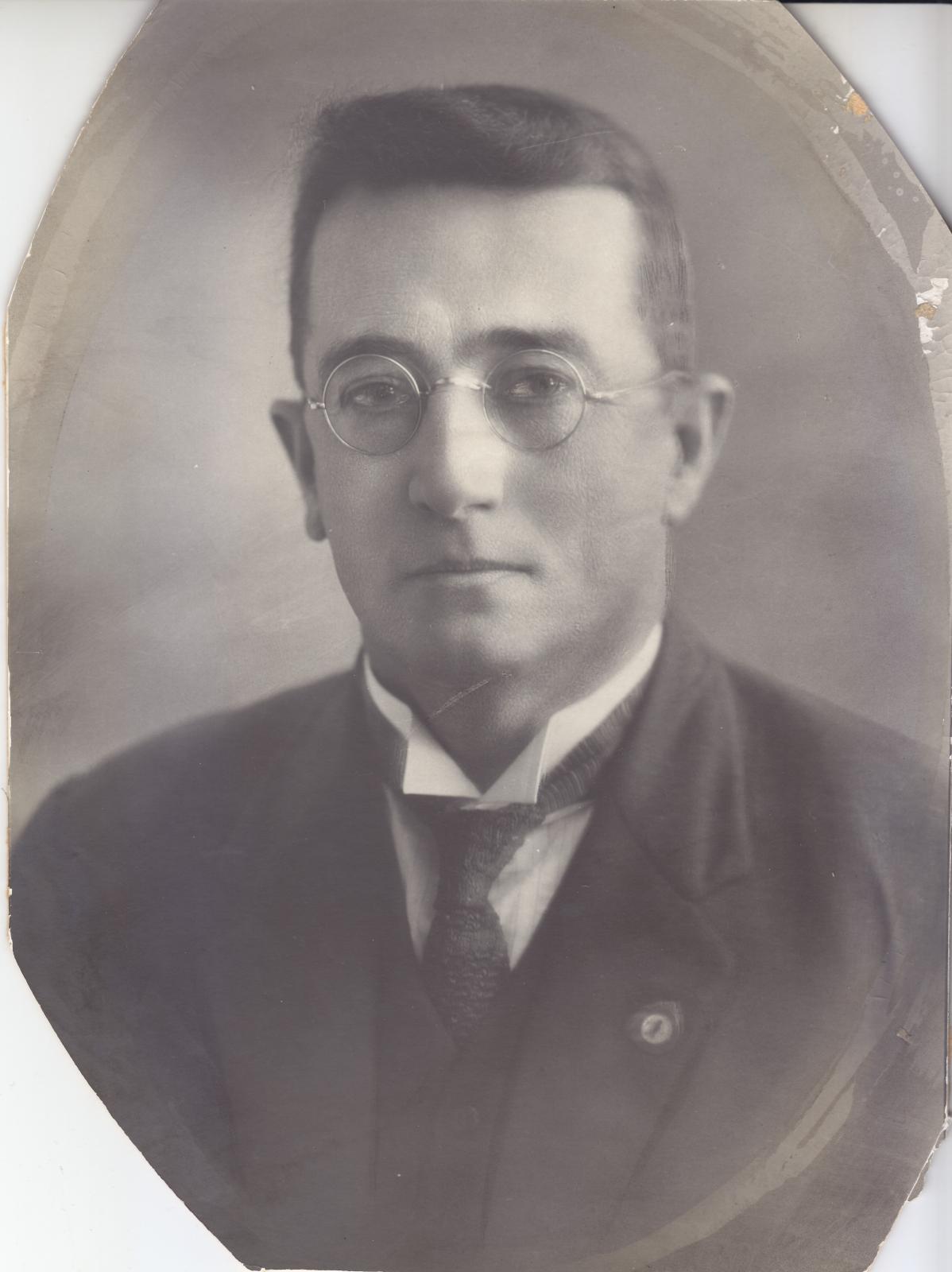 B/W portrait photograph of a middle-aged man wearing round glasses and a suit & tie