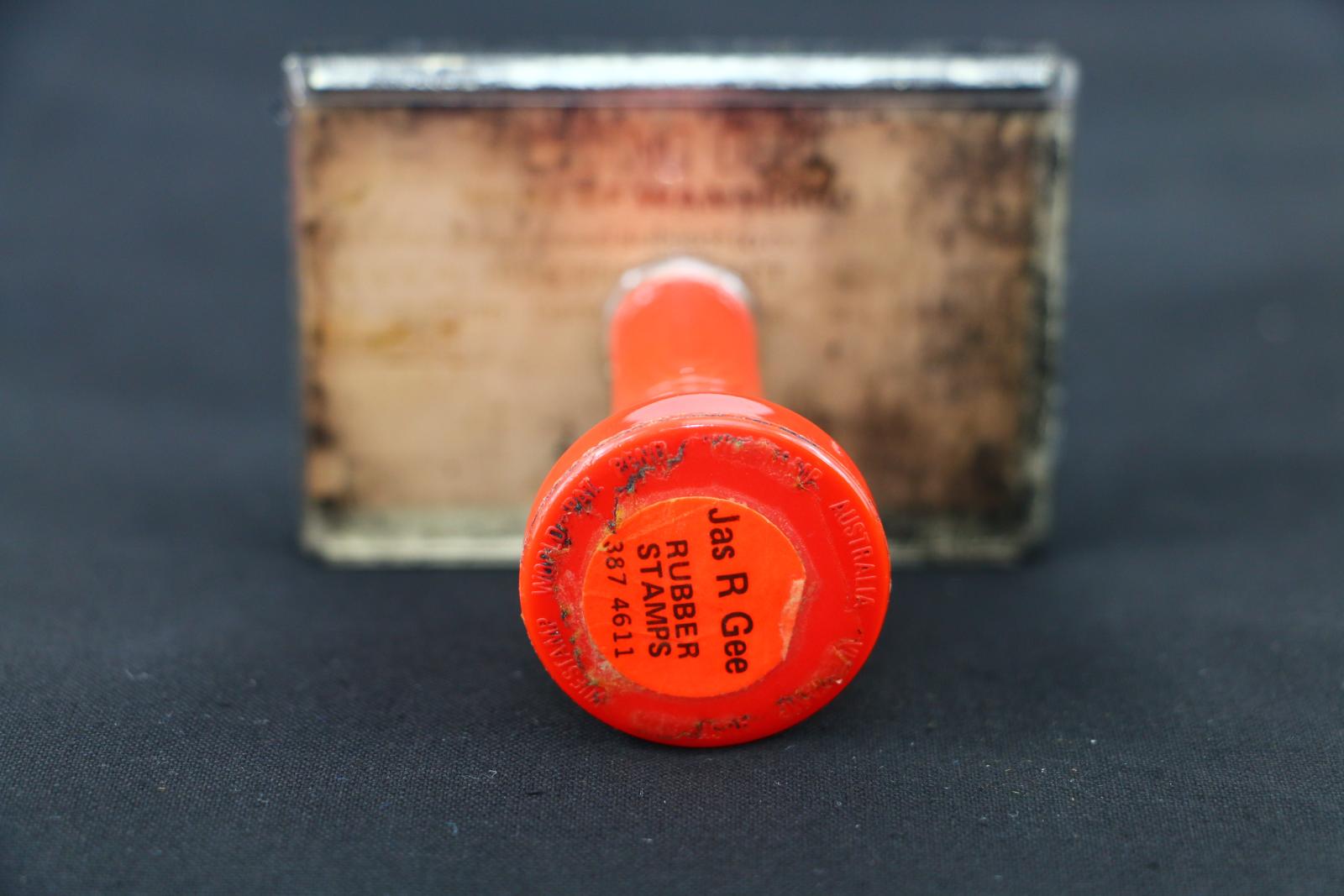 A clear Perspex stamp with red handle. A view from the top. The stamp has black ink on the top of the Perspex. 