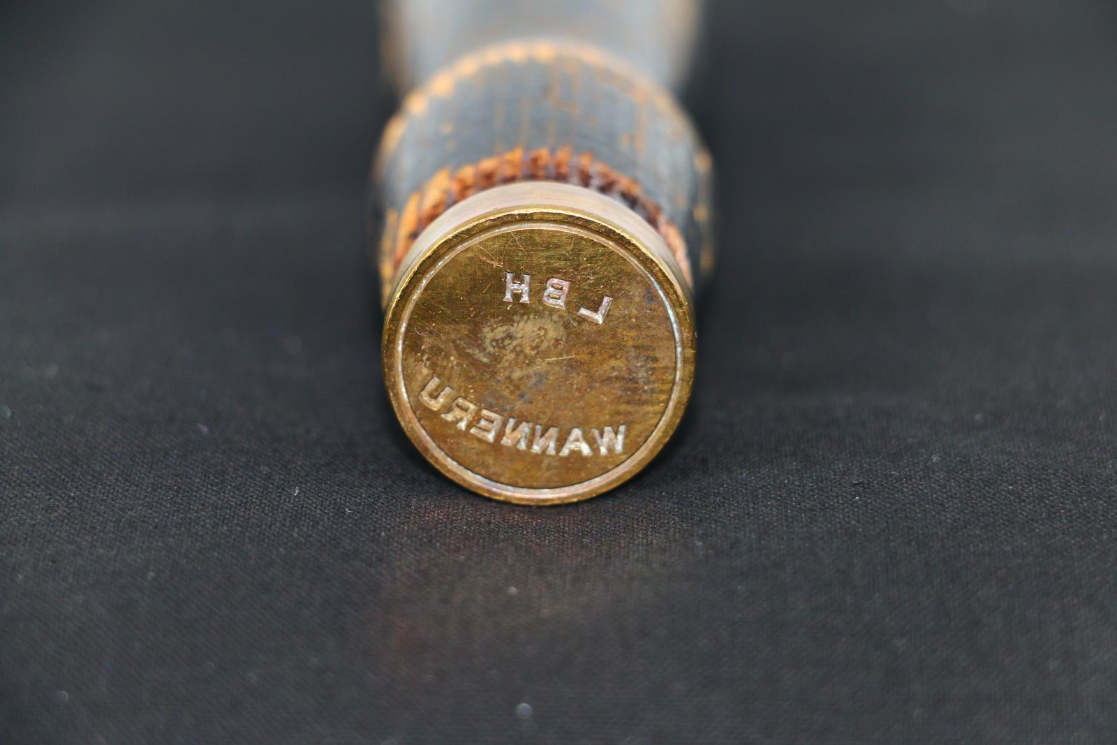 A brown wooden handle, painted black, wax seal that is shaped for hand use. The paint on the wooden handle is peeling away. A brass screw is located on one side of the wooden handle. A solid brass circular seal with stamp imprint is located at one end of the object.