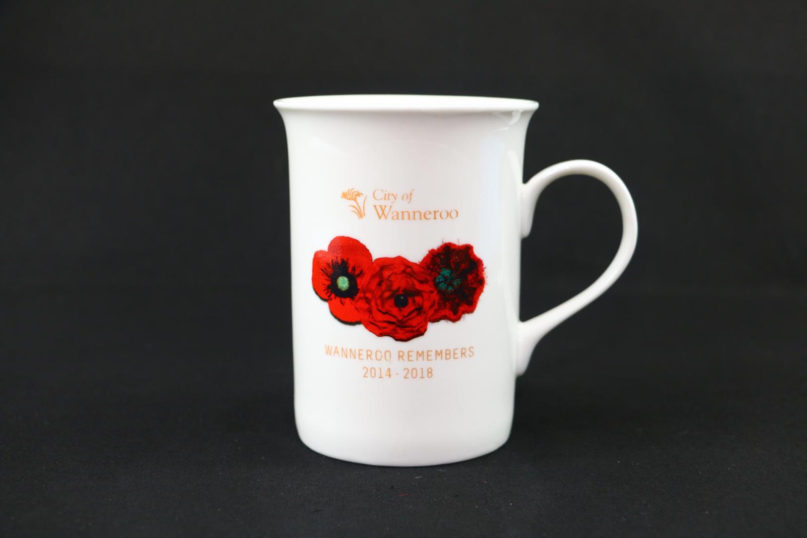 White mug with three red poppies design on one side. The City of Wanneroo logo appears above in gold lettering and below is the capitalised text 'WANNEROO REMEMBERS/1914-1918', also in gold lettering. On the outer base of mug, the branding 'Maxwell Williams' is written in red and black lettering.