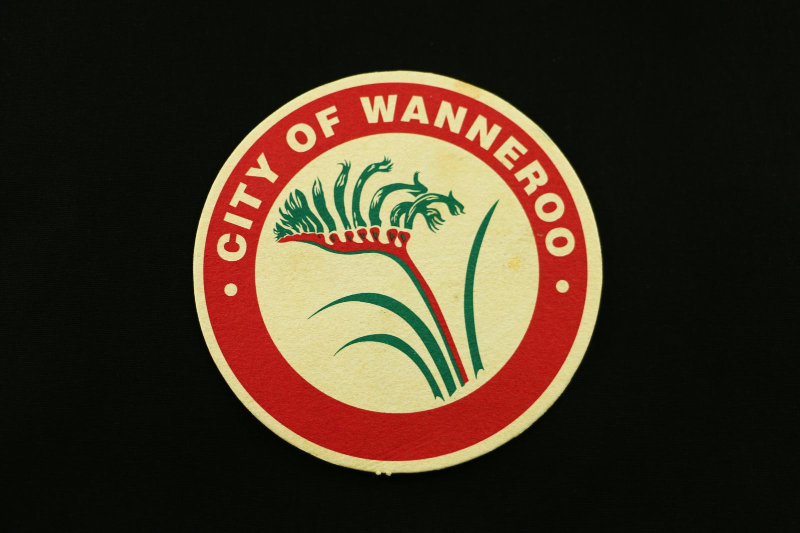 Round coaster with a red border and red and green kangaroo paw logo in centre, 'CITY OF WANNEROO' printed in border in white text.