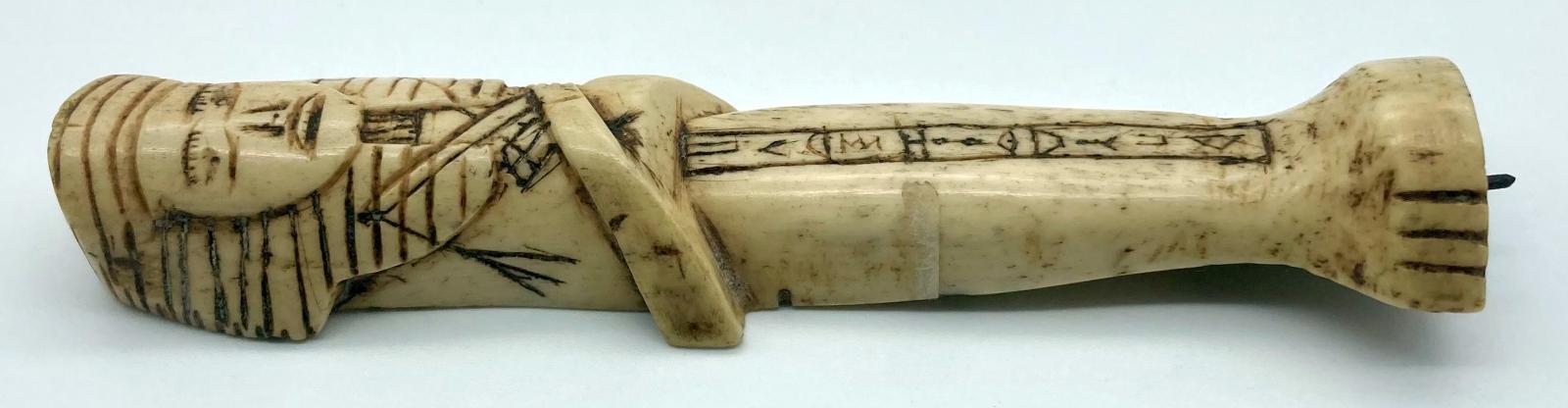 Side view of carved camel bone in the form of an Egyptian shabti
