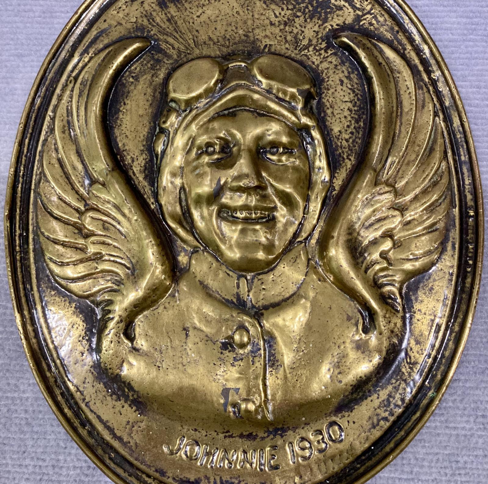 Close up of Front of pressed brass wall plaque featuring the relief portrait of aviatrix Amy Johnson