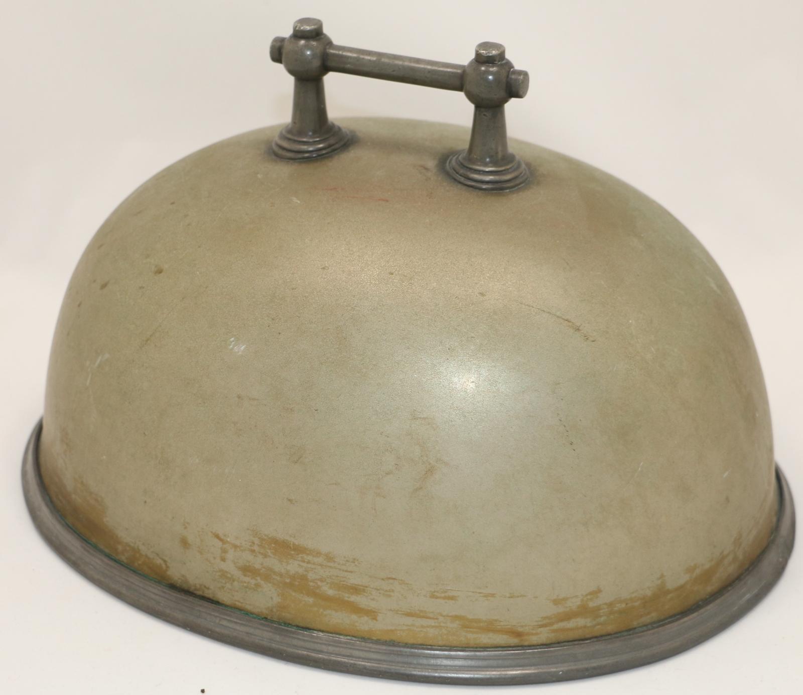 Oval solid argent metal heavy food cover with a solid metal square shaped handle attached with wing nuts to the top and a solid edging around the base.