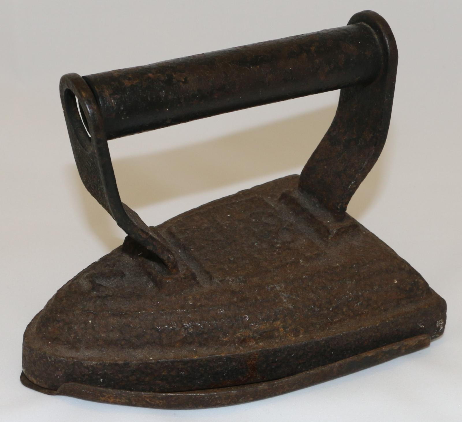 Hand held stove top flat iron with hollow metal cylindrical handle with dent on top attached to cast iron brackets, painted black and welded to iron base. Base heavily corroded. Slightly pointed front with broad flat base.