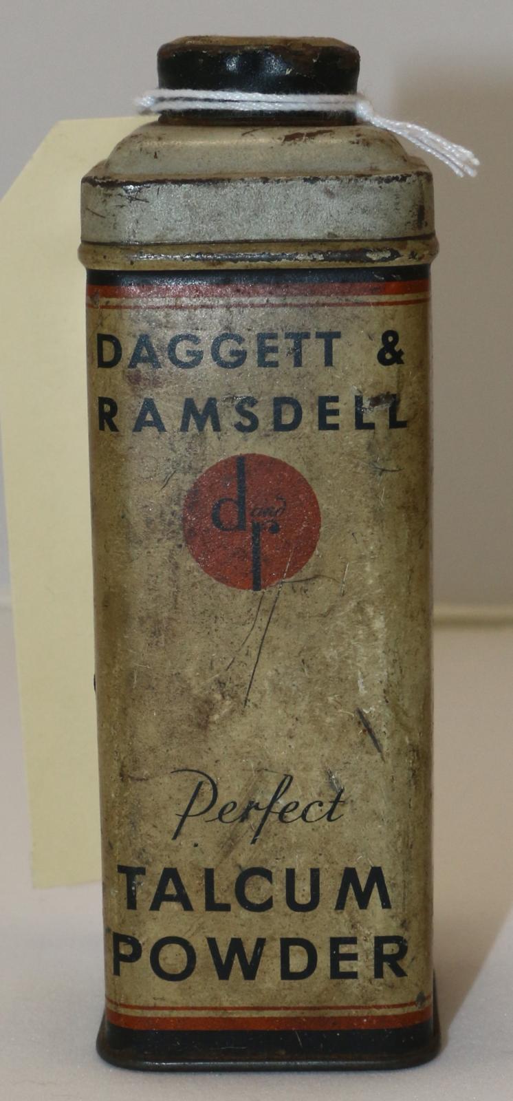 A rectangular beige, red, black and cream coloured tin with six holes punched on top of lid of a container used to hold talcum powder.