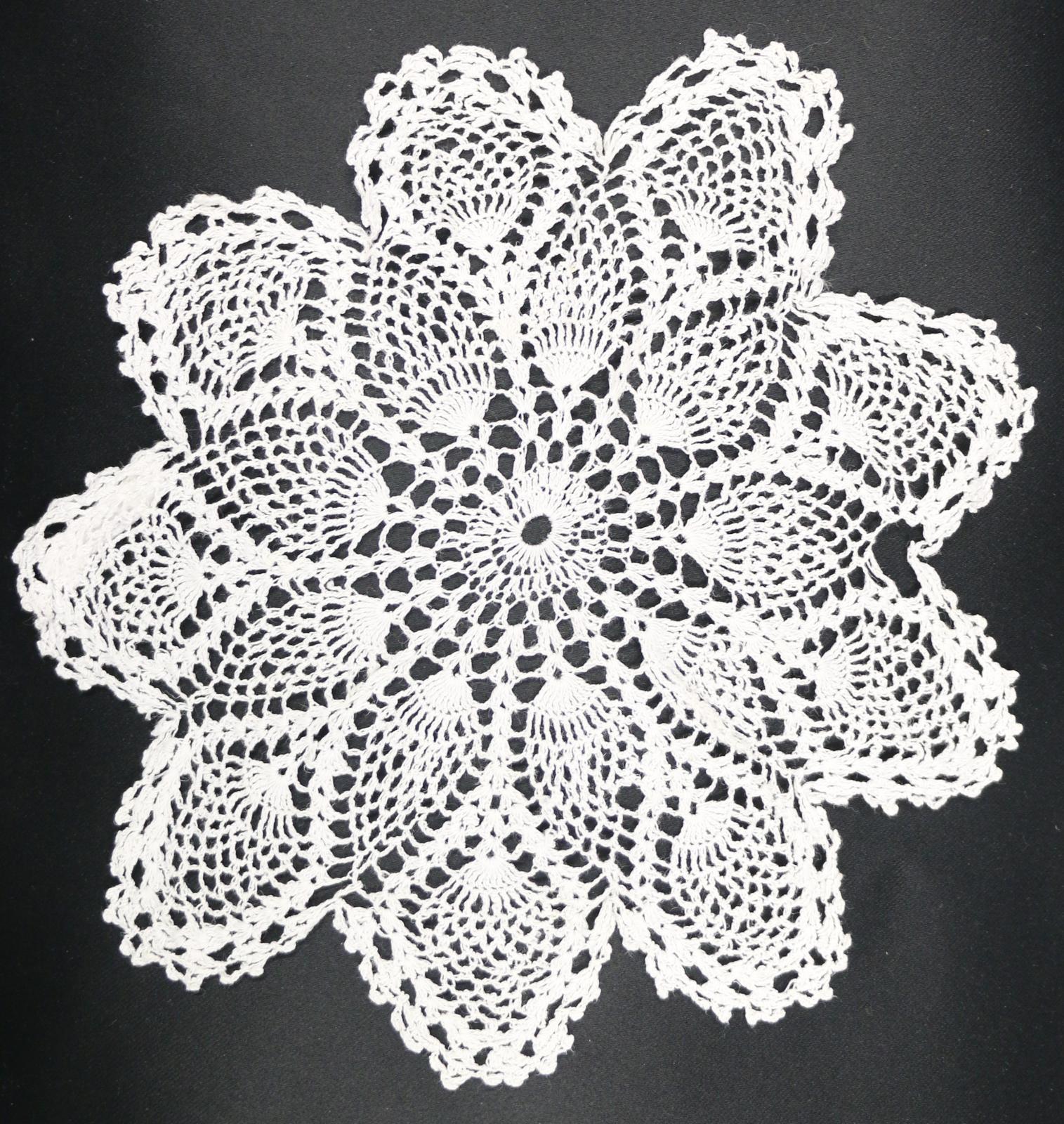 Cream coloured, round, crocheted lace doily with 9 shaped petals extending from centre.