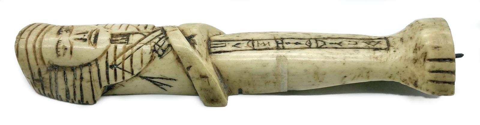 Side view of carved camel bone in the form of an Egyptian shabti