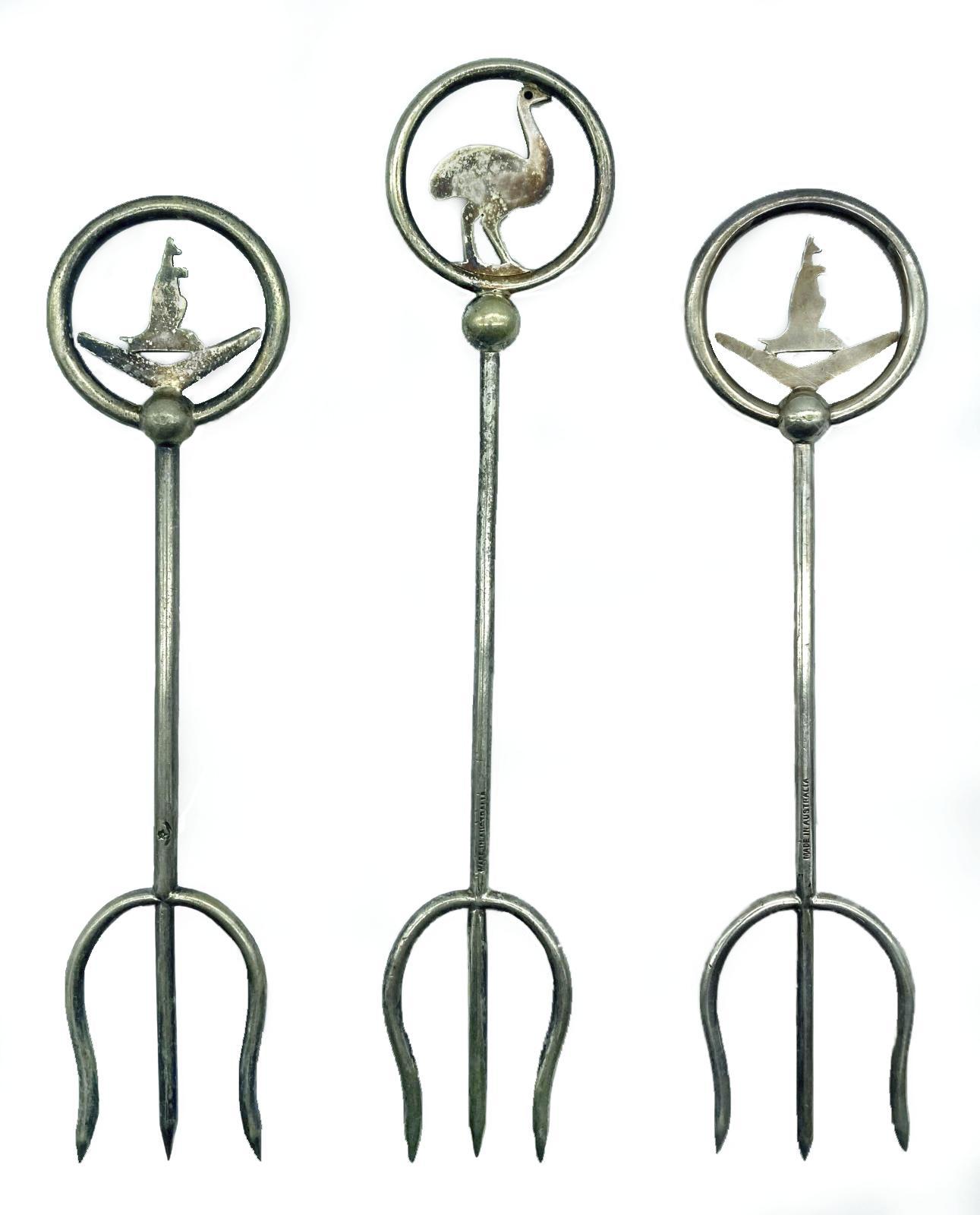 Reverse of group of three silver plated trident bread forks with decorative tops