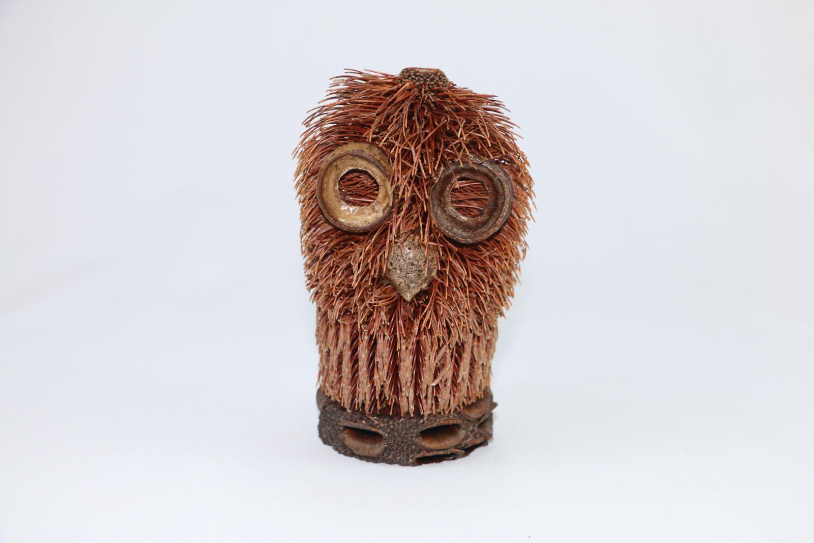 An owl figure made from plant material on a circular piece of wood.