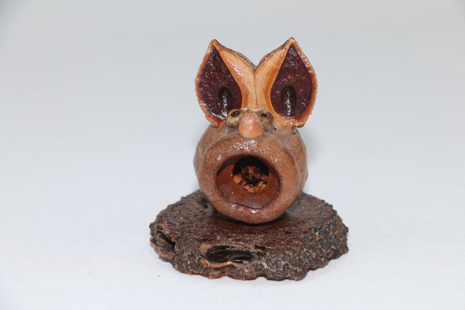 Small mouse figure made from a gumnut and other plants, the figure is on a small circular wooden base.