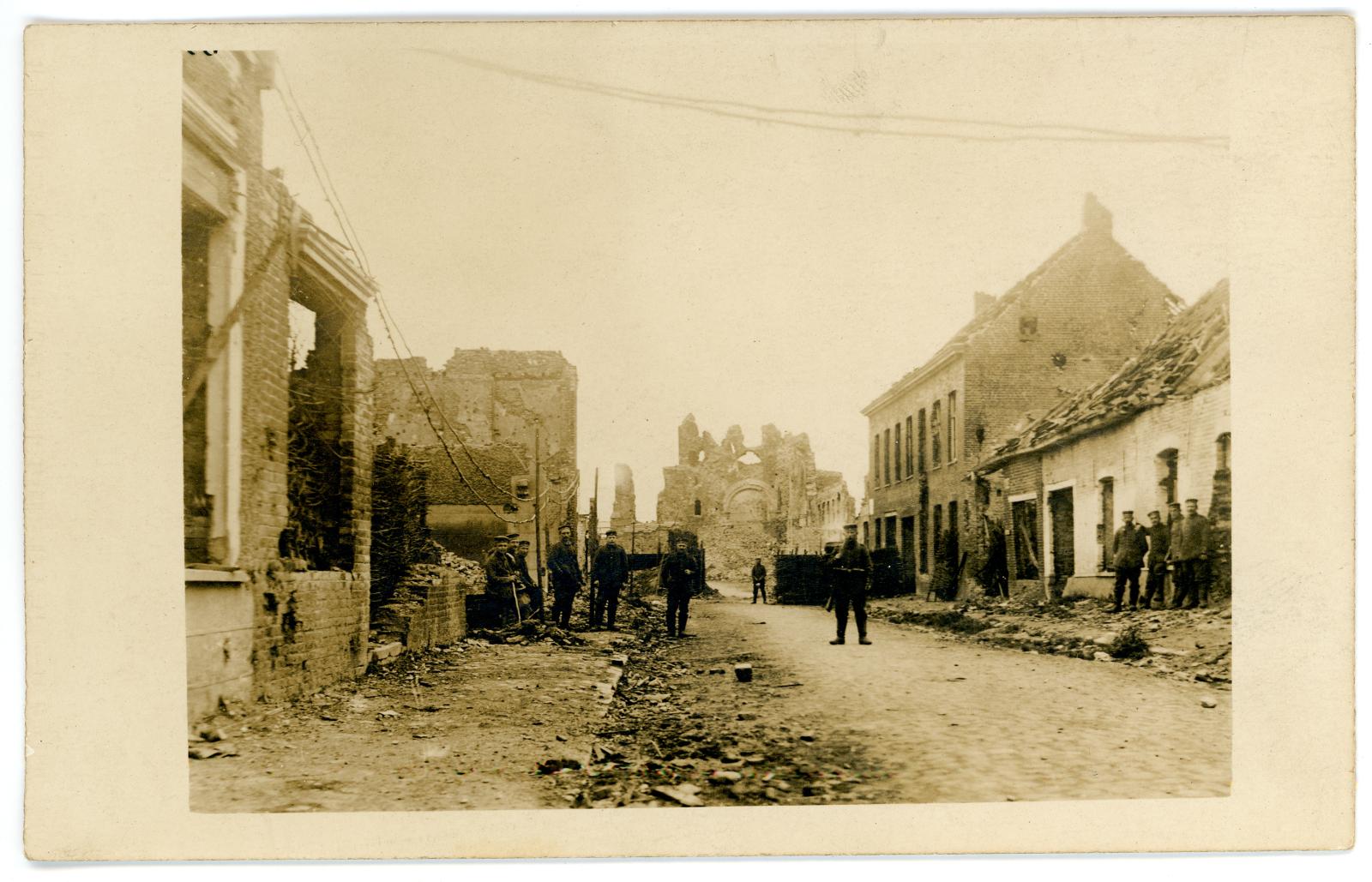 Photo postcard showing soldiers standing & sitting amongst bombed building ruins.