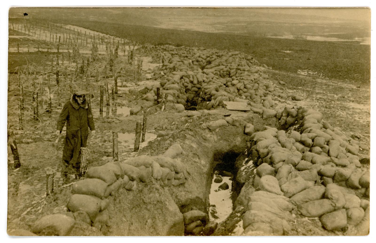 Photo postcard showing sand bagged trenches and soldier.