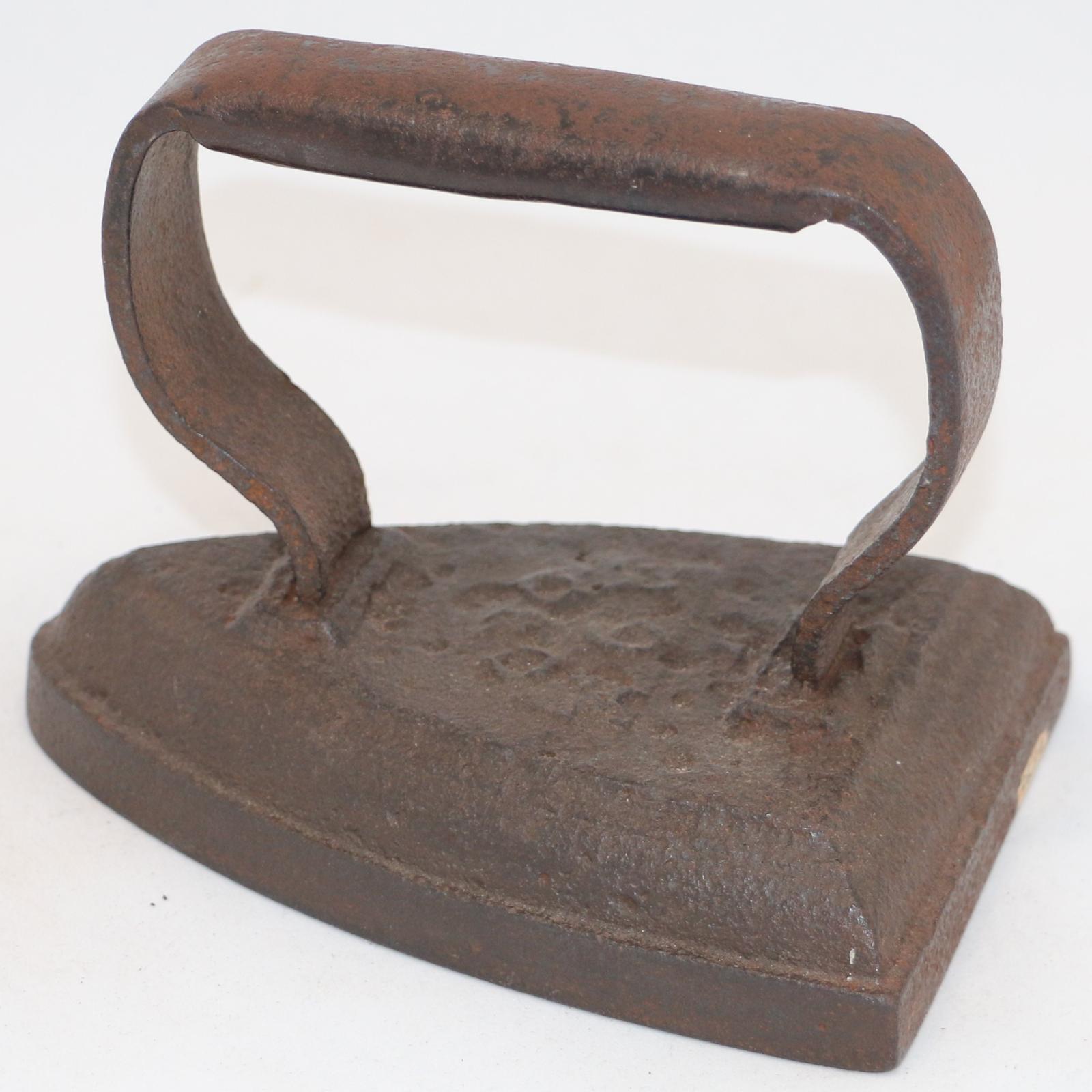 Hand held stove top flat iron with metal handle on top, welded to iron base. Base heavily corroded. Slightly pointed front with broad flat base.