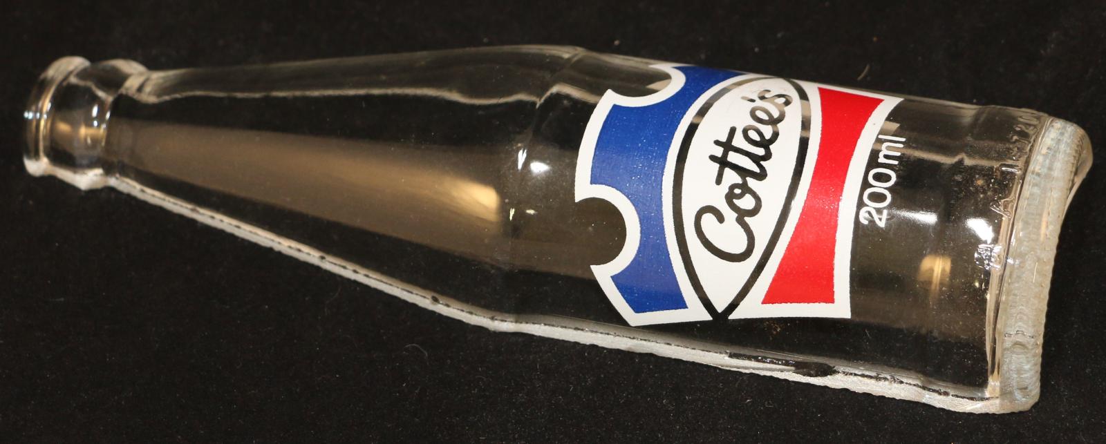 Cylindrical, clear glass, Cottee's bottle. Round cylinder of clear glass, with a thick base, and tapering from halfway up the bottle to a smaller round opening at the top. The entire bottle is cut in half vertically. Printed on the outside surface of the bottle in white lettering is 'Cottee's/'TM Regd'/THIS BOTTLE REMAINS / THE PROPERTY OF / PASSIONA BOTTLING CO. / (PERTH) LTD. / PLEASE RETURN FOR REFUND'