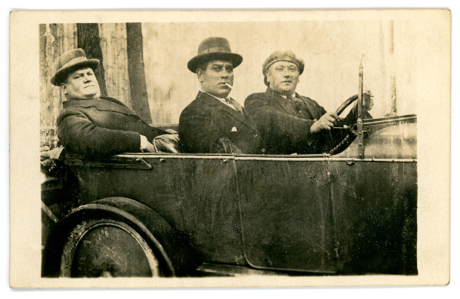Three men in civilian clothes sitting in open top vehicle.