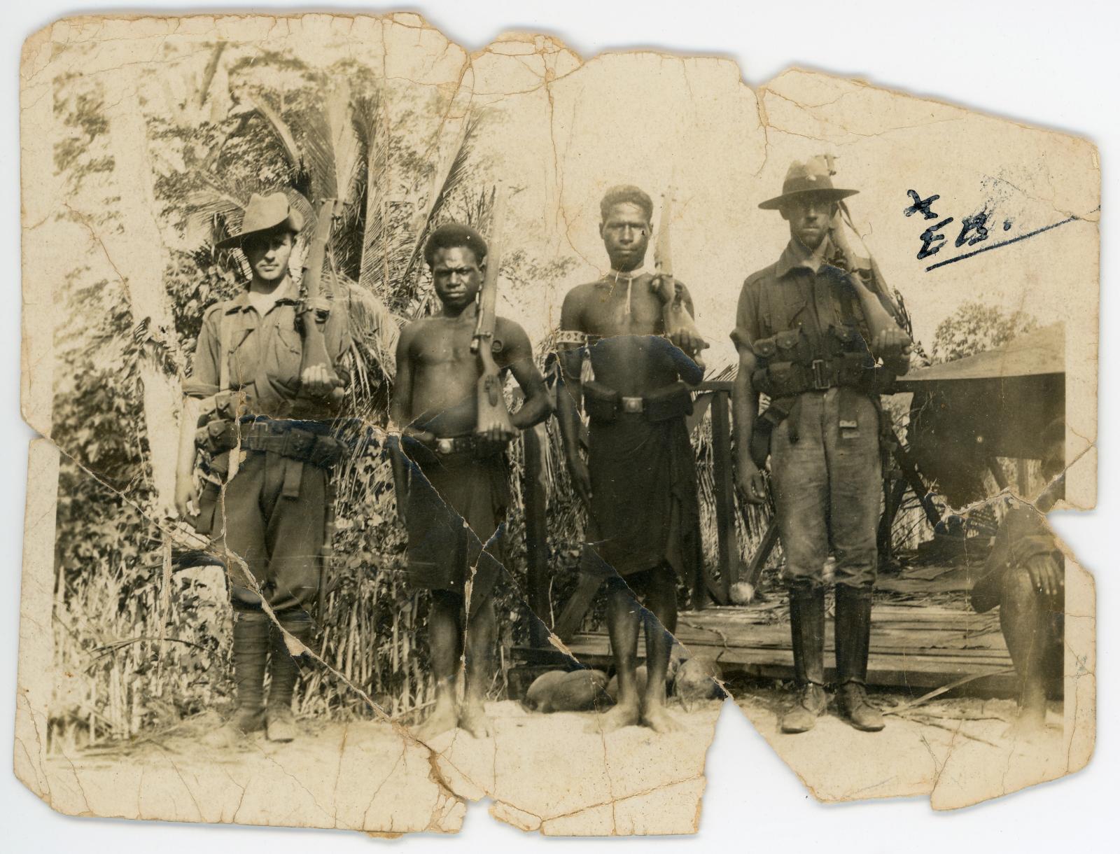 Two Australian soldiers and two Papuan soldiers holding rifles over left shoulder.