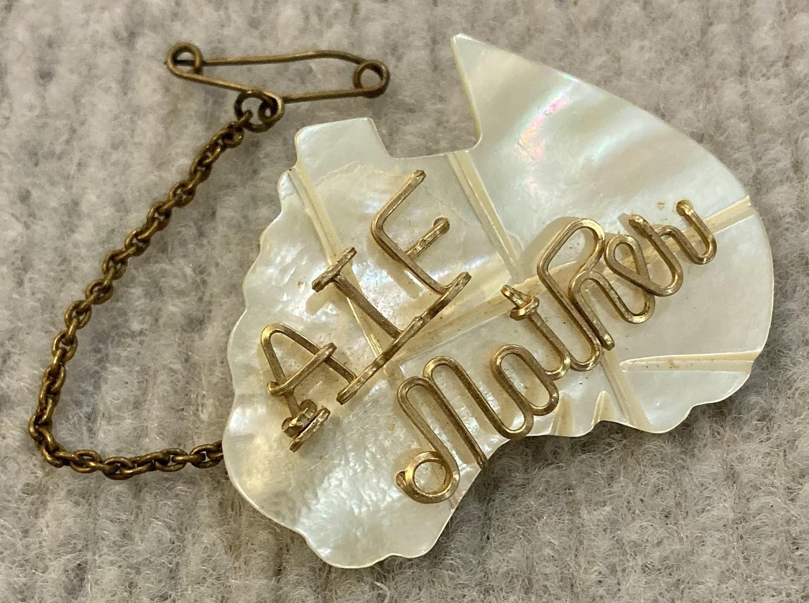 Angled view of mother of pearl A.I.F. sweetheart brooch with attached safety pin