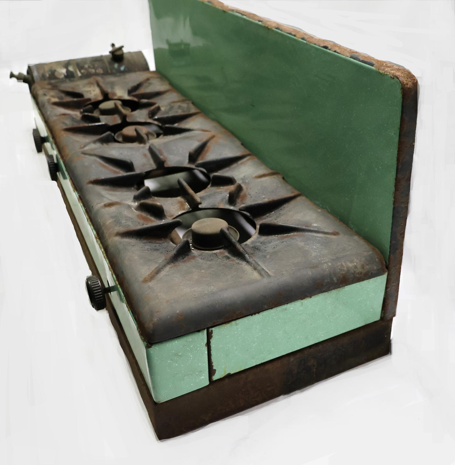 The front of the cooker which is green and cast iron, there is a fuel tank on the left hand side and three round black knobs on the front. Four burners on the top.