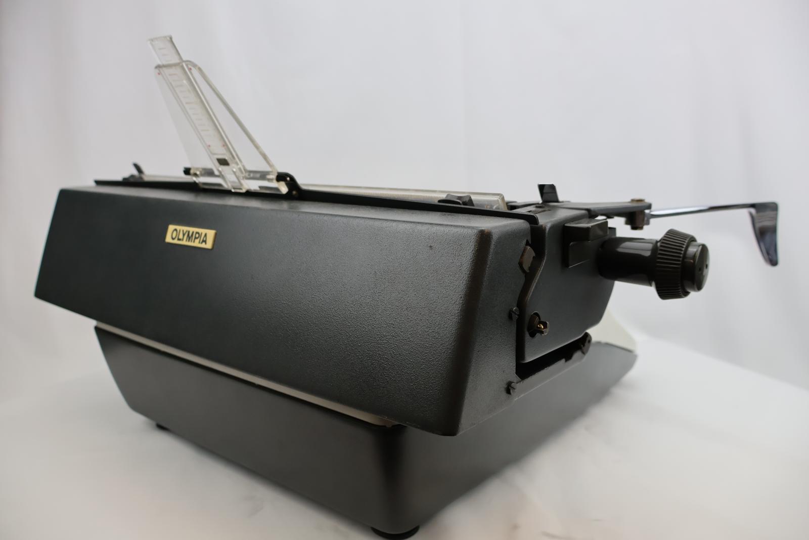 White front with grey keys. A grey carriage with clear plastic paper support. On the carriage is a silver metal line spacer lever. Rectangular shape, four feet on the bottom corners. Raised area in the middle same level as carriage. The front tapers down at an angle for the type keys.
