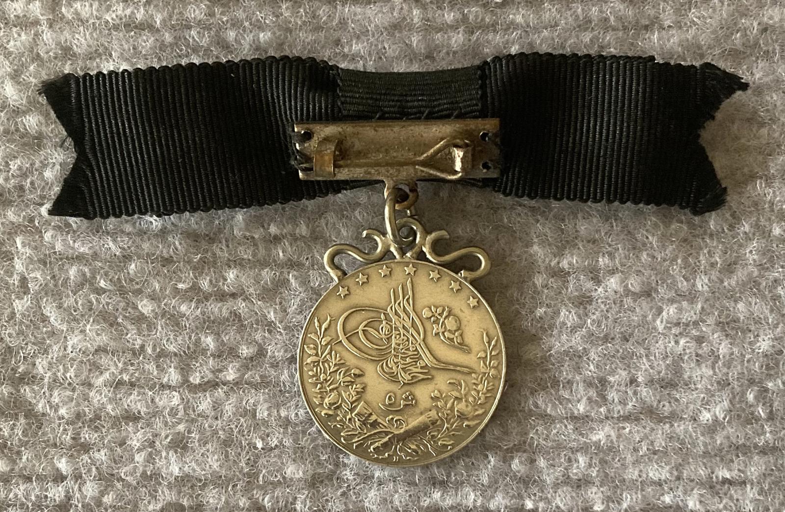 Reverse of identity badge made from coin suspended on black bow brooch