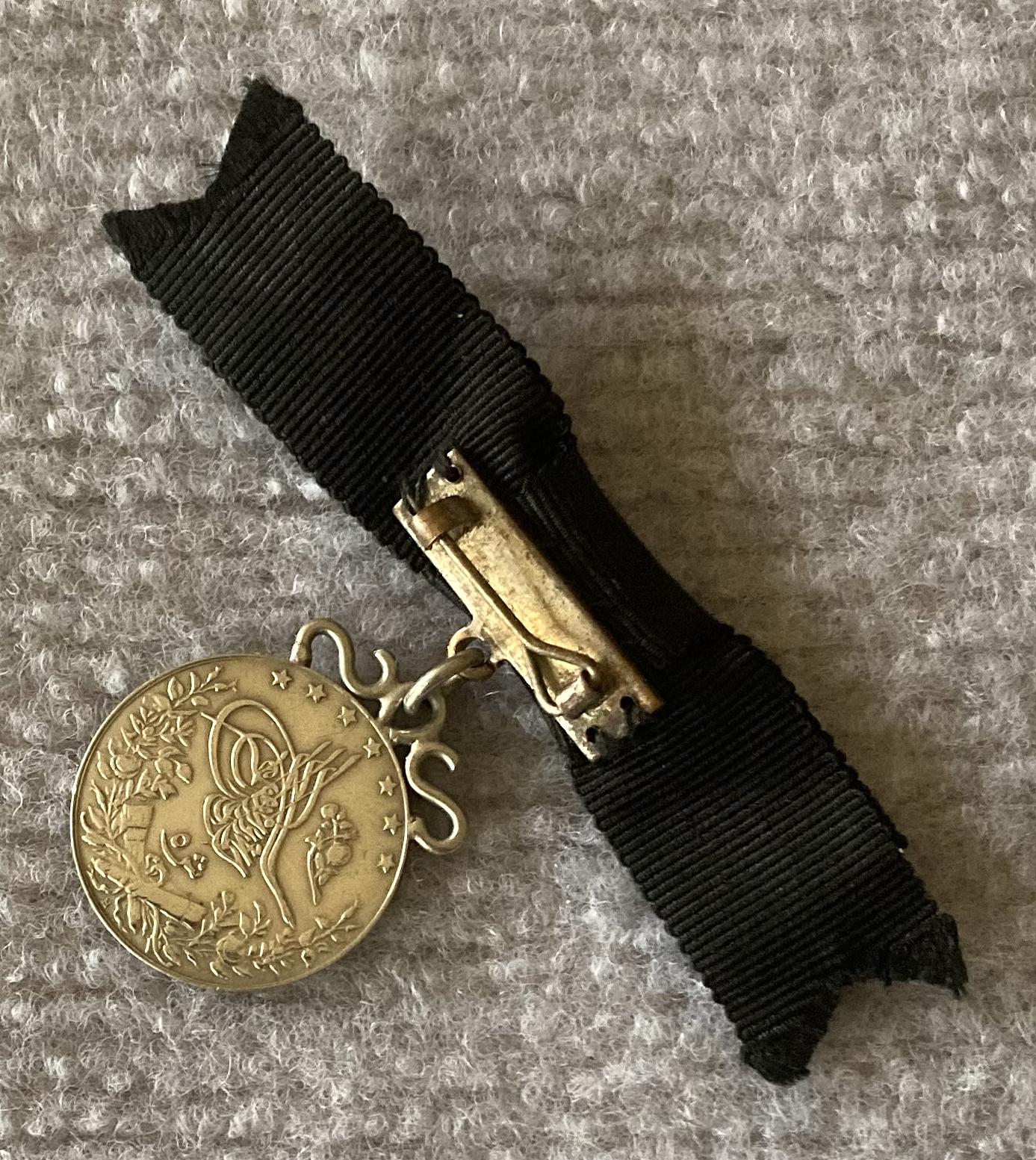 Angled view of reverse of identity badge made from coin suspended on black bow brooch