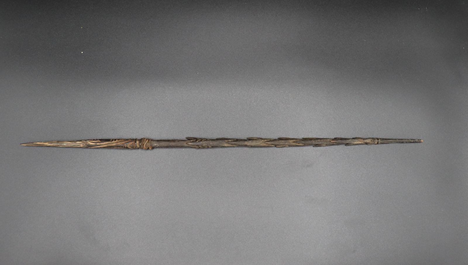 A dark brown, barbed wooden spear approximately 35cm in length.