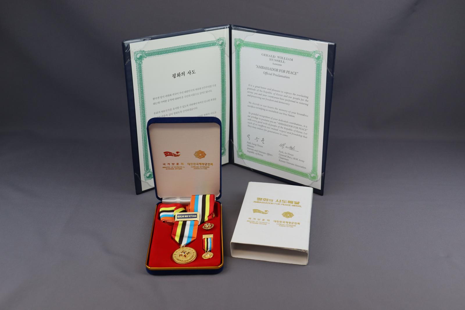 Round gold coloured medal attached to a stripped, multi-coloured ribbon, in a case.