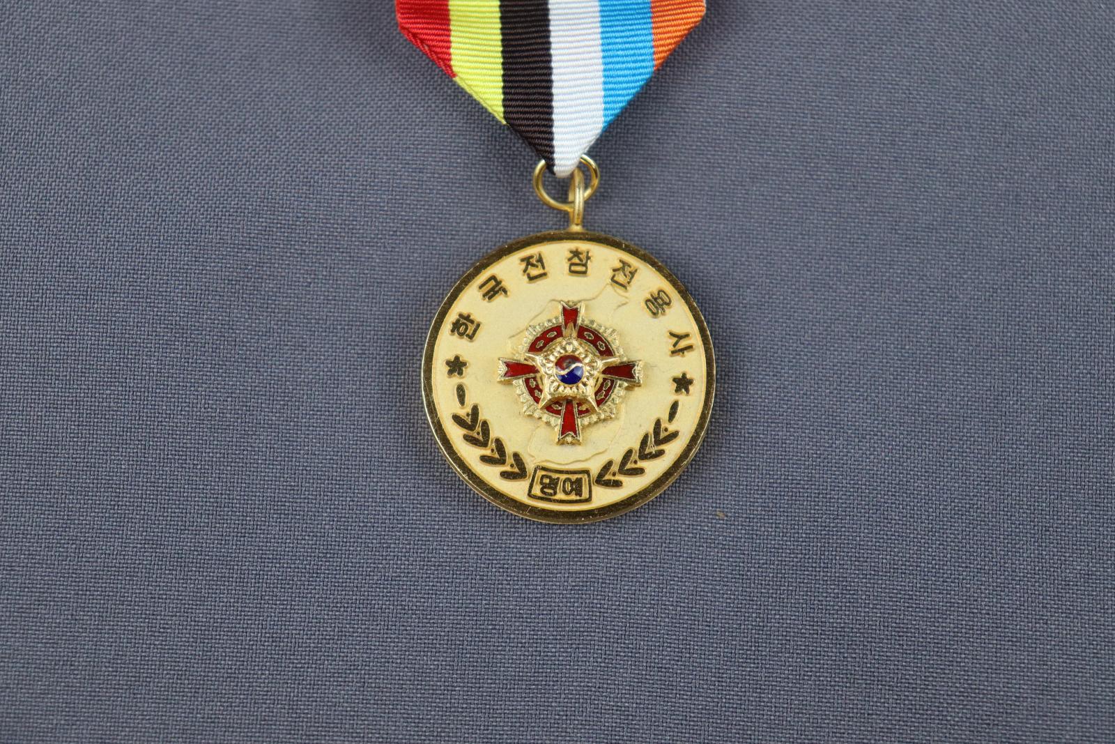 A round, gold medal with a small loop at the top attached to a striped, coloured ribbon.