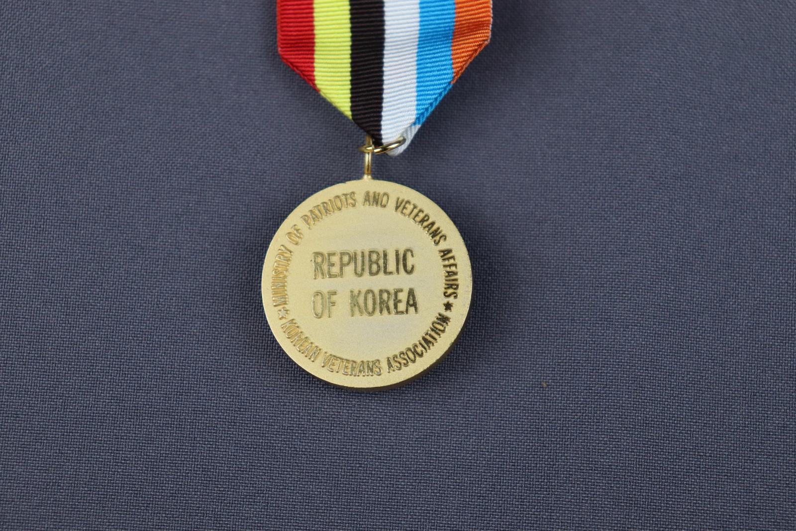 Round gold coloured medal attached to a multicoloured stripped ribbon.  