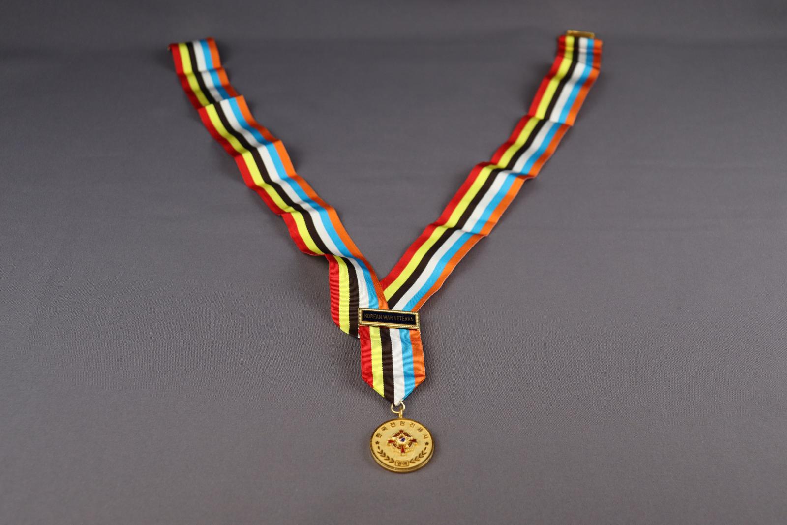 A round, gold medal, with the multicoloured ribbon it's attached to laid out on display.