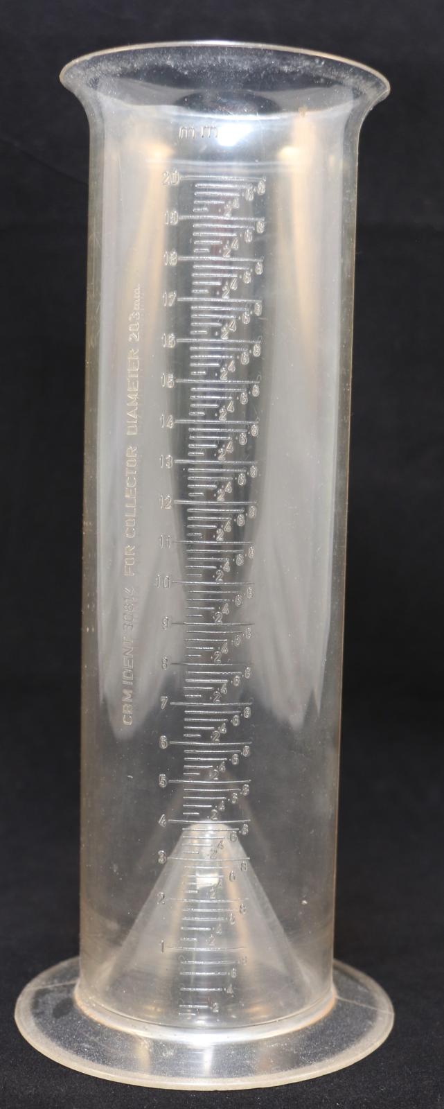 A tall, cylindrical, clear plastic, with 0 to 20mm scale measurements on a rain gauge. The base of the cylinder stops at the edge of container to form a conical shape within, where at the tip of the cone is a length of stem of spike. The plastic container which has joins on both sides also has a flared rim. On the front are raised prominent graduations of measurements starting in increments of 0. - .2 -.4 -.6 -.8, 1mm to the maximum of 20mm.