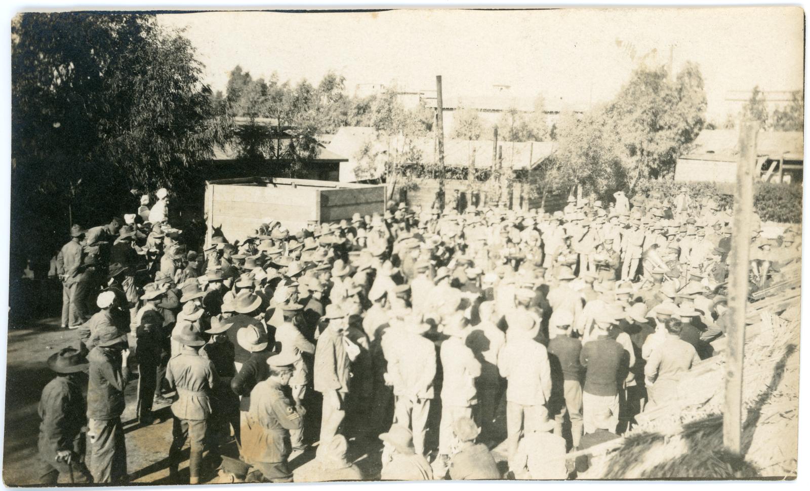 Photo shows a military band playing to a large group of Australian soldiers.