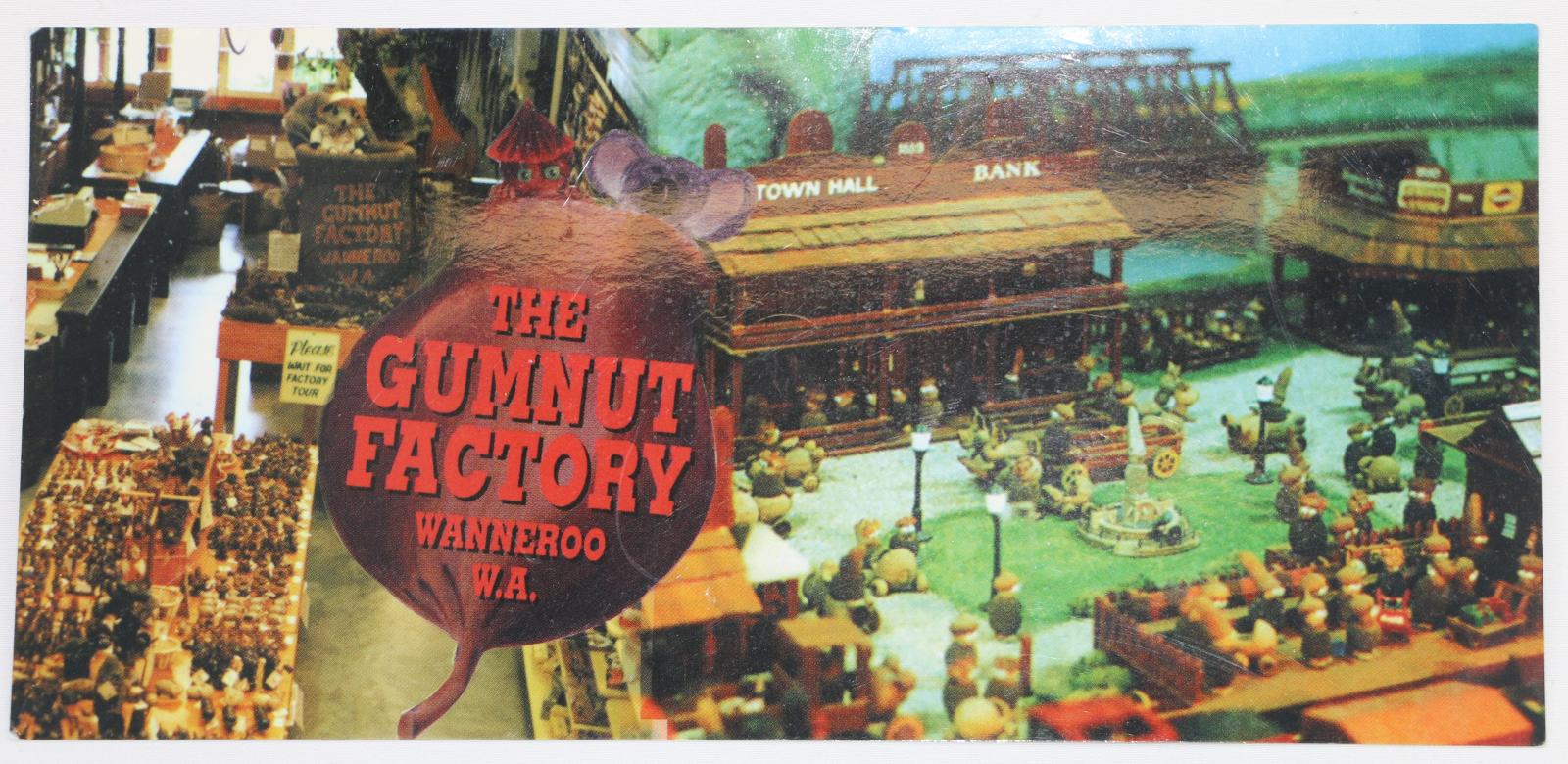 A rectangular postcard with a glossy image, on the left hand side is an image of a store and on the right hand side is an image of a model village. There is an image of a large gumnut with two figures peaking out from the top, a gumnut person and a koala, the gumnut has the following text 'THE GUMNUT FRACTORY WANNEROO W.A.'