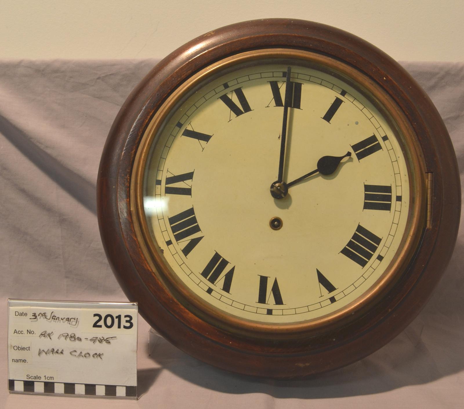 A round wall clock with roman numerals on a cream-coloured face.