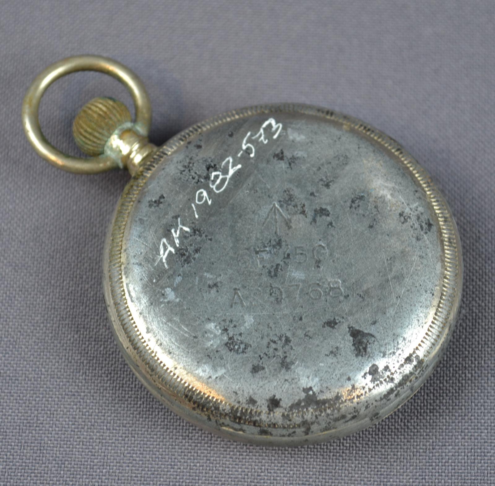 The silver-coloured back of the pocket watch, marked with British Airforce engravings; 6E / 50. A29768