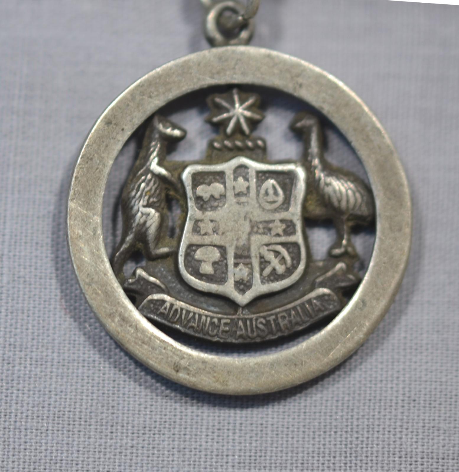 A 2.5cm - 3.0cm diameter medal, showing a Kangaroo and Emu either side of a shield (The Australian Coat of Arms) above a banner reading "Advance Australia". Above the shield is what looks like a small length of rope and a 7-pointed star.