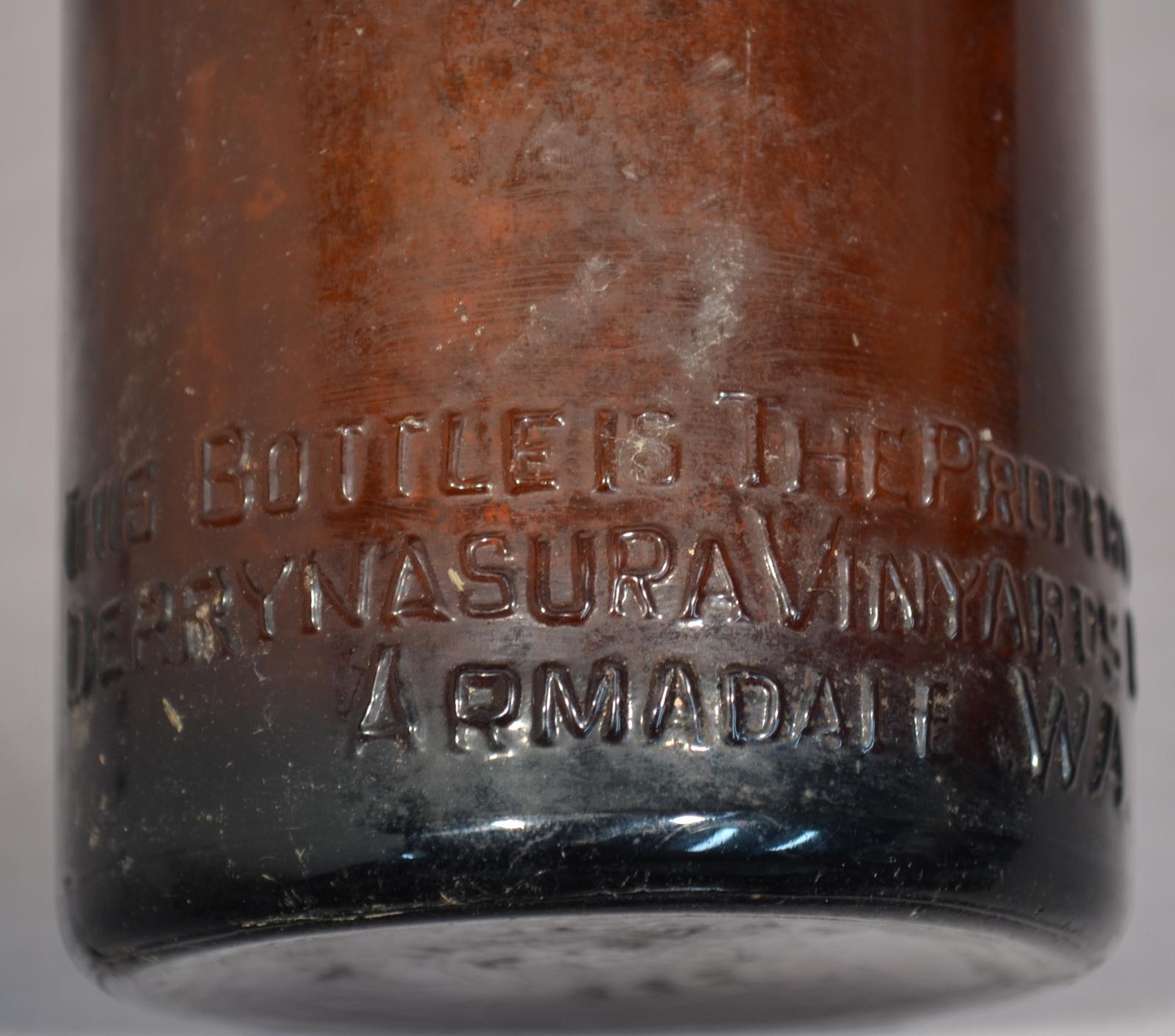 molded brown text on bottom edge of brown glass bottle 'THIS BOTTLE IS THE PROPERTY OF / DERRYNASURA VINEYARD LTD / ARMADALE WA]. Also on the base and the molded numbers 8432 & the letters G / M inside a larger A