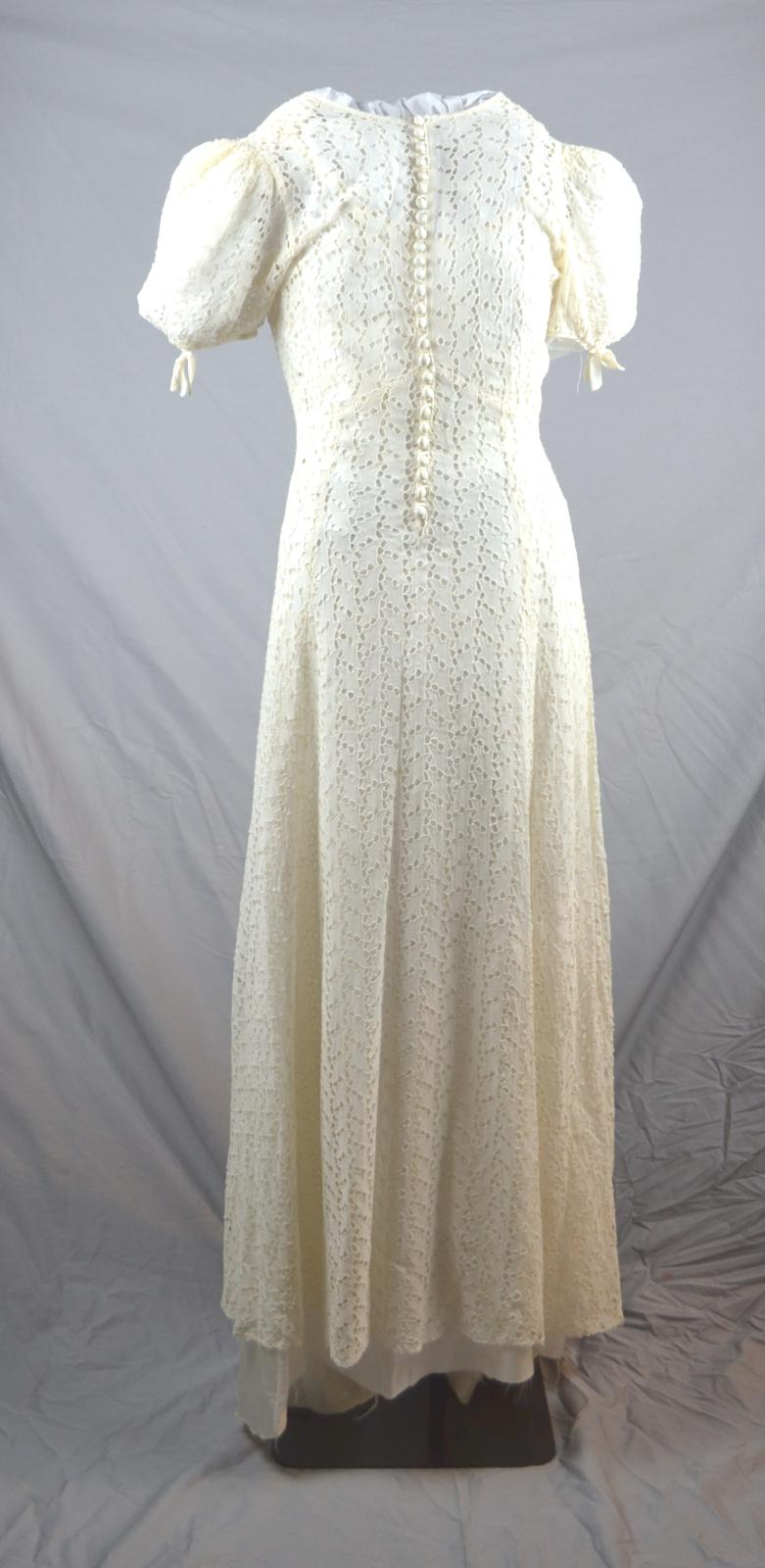 The back of a full length, cream broderie anglaise wedding dress.