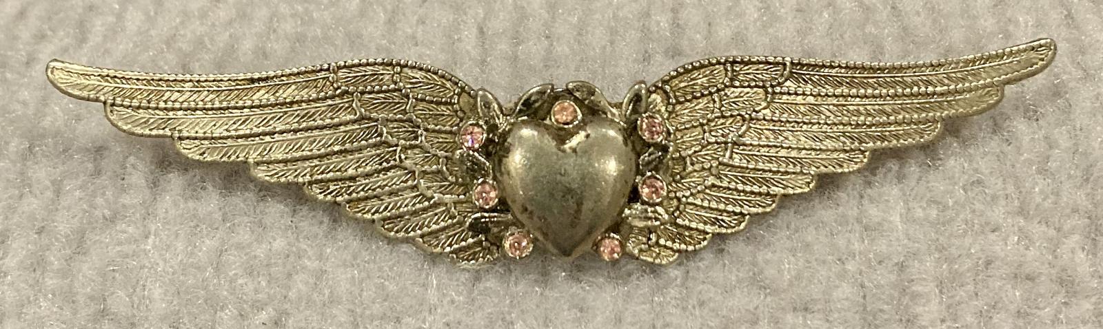 Silver tone sweetheart brooch featuring wings with central heart and pink stones