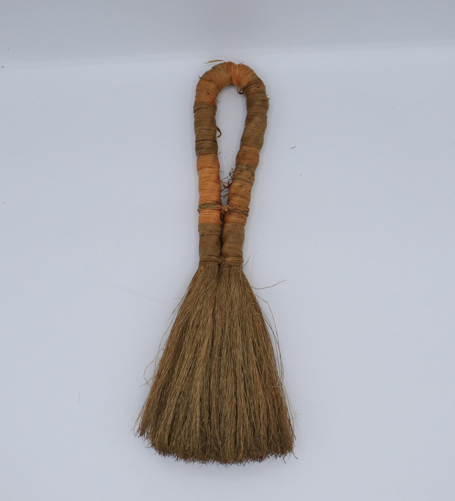 A small grass/reed brush, folded at the middle to form a looped handle.