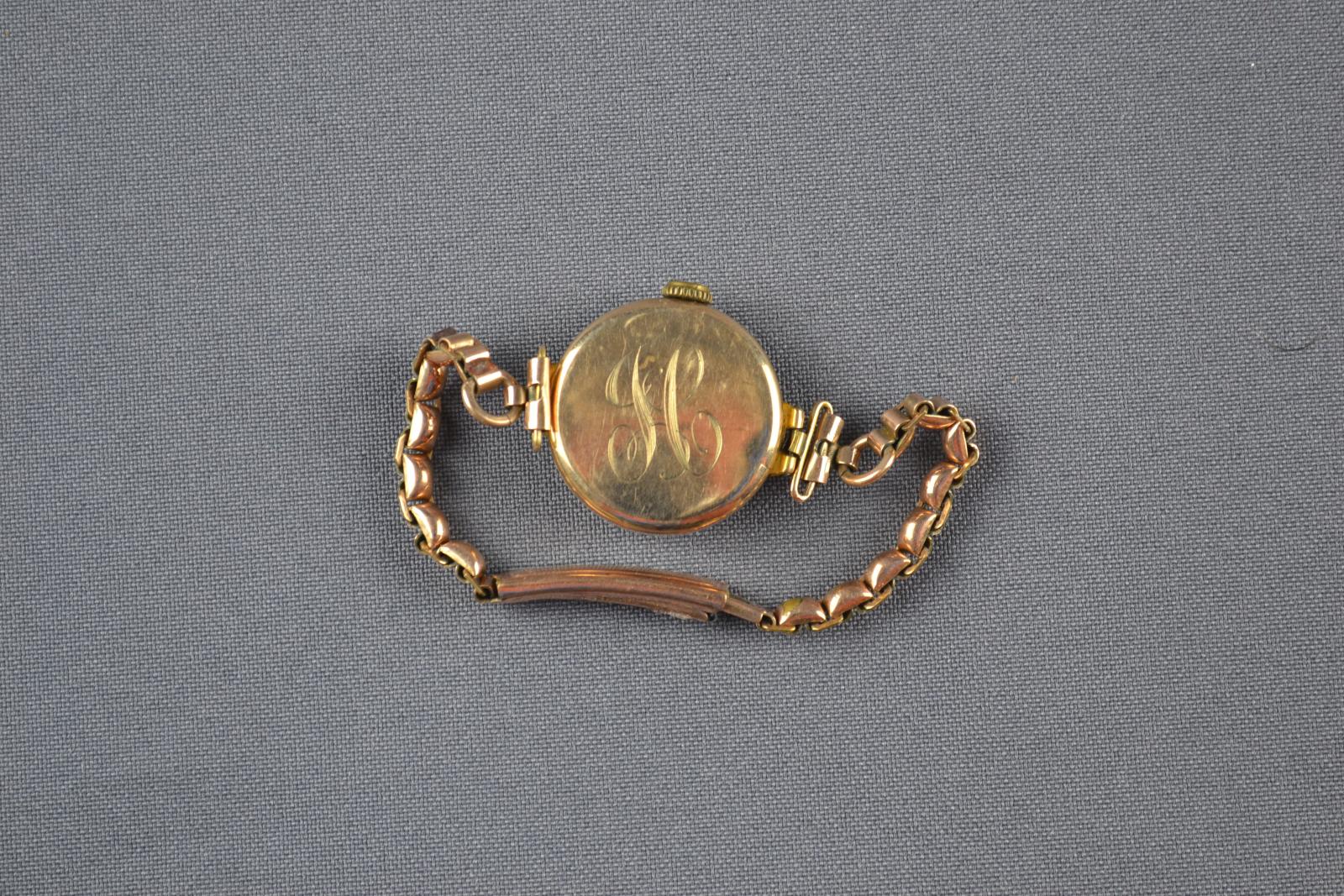The backside of a gold-coloured wristwatch with a belcher-chain wristband. Engraved with the initials I and C.