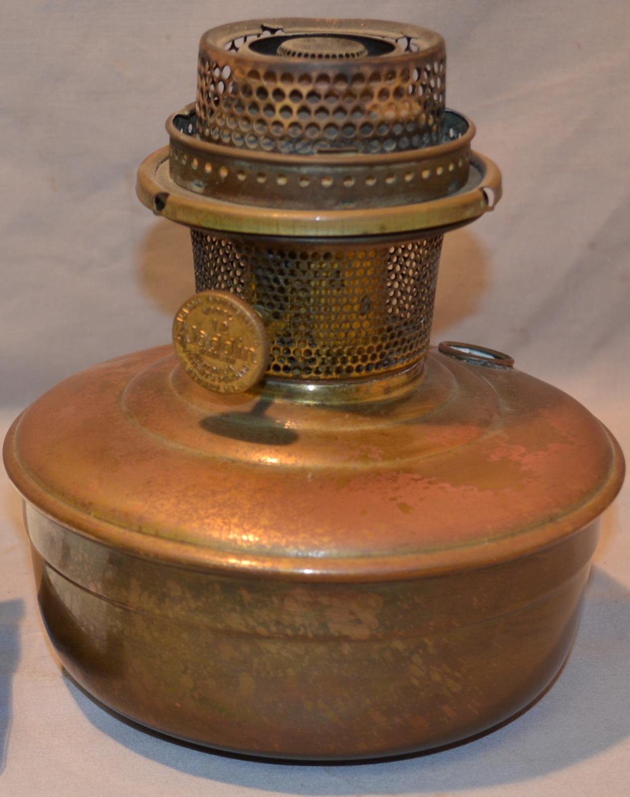 A round, copper-coloured lamp with a wide, deep reservoir as the base and perforated metal cylinder of differing widths, protruding from the centre.