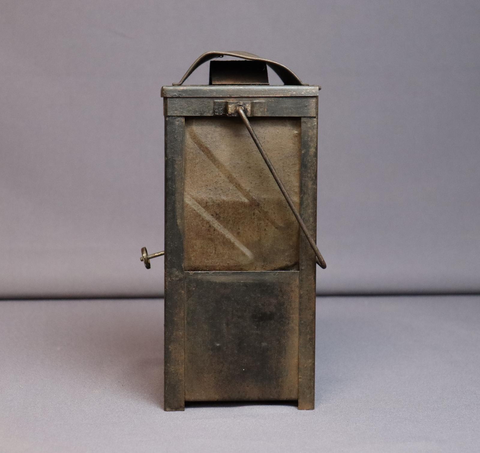 Rectangular metal case with a rectangular window taking up the top half, covered on the inside by a pitted piece of metal. The squared handle and burner control knob are both visible from this angle.