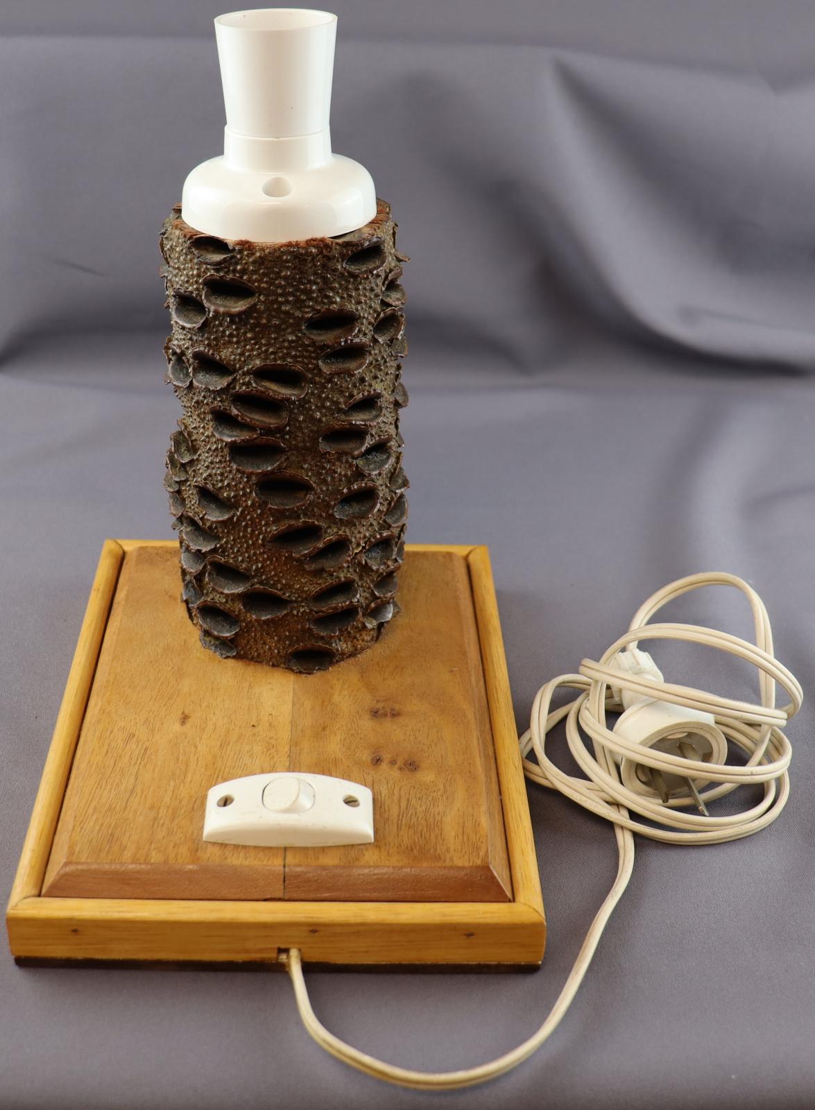 Rectangular wooden base with a Banksia nut stand housing a plastic light fitting on top and a plastic on/off switch beside it. A cable with a three-pin plug protrudes from the side.