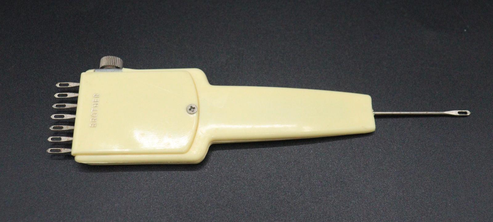 A cream-coloured plastic cartridge with 7 short, looped needles on one end and a single, longer looped needle on the other.
