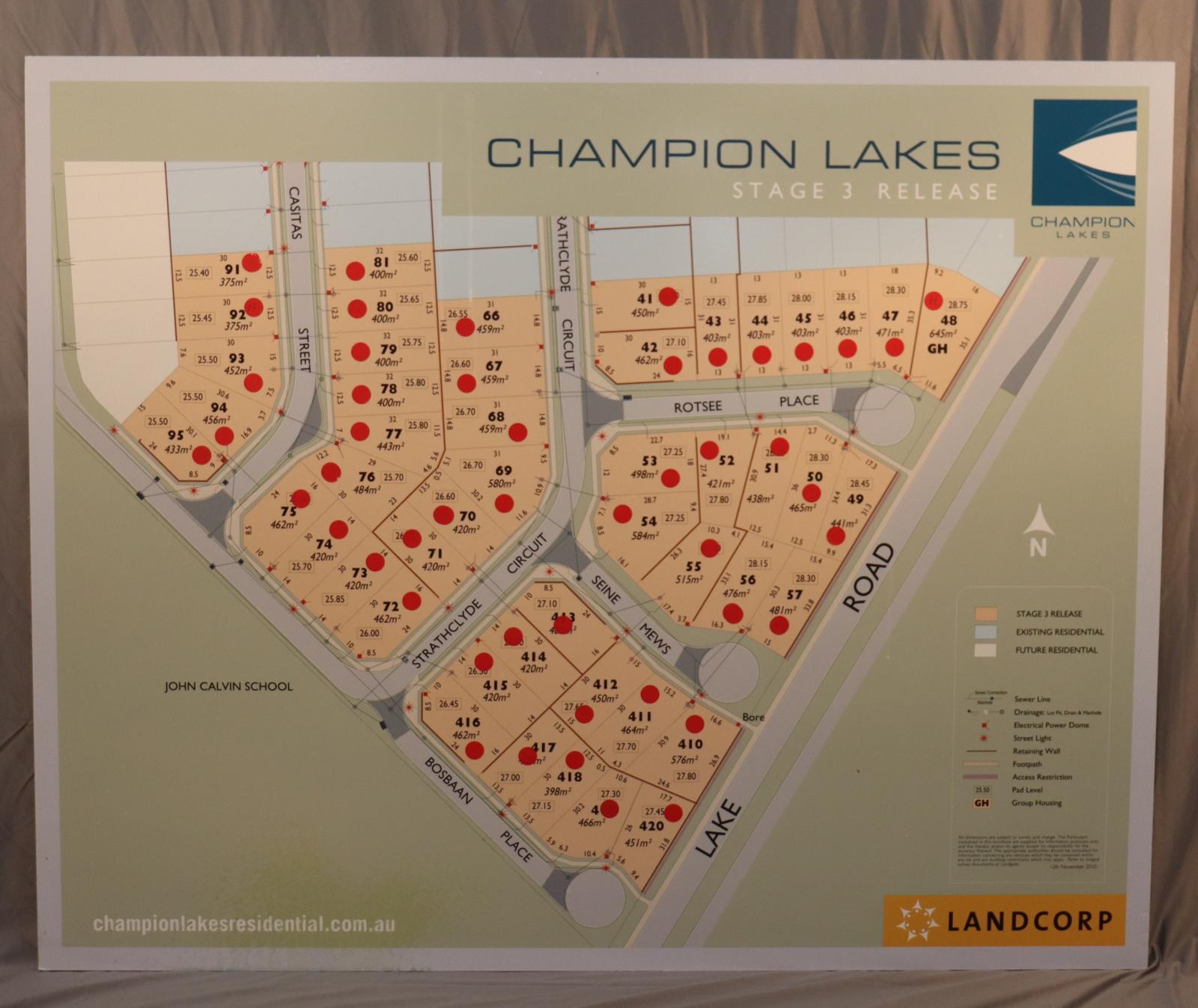 Sheet of wood attached to polyester form sheet. Rectangular. Sage-green background colour with light blue strip around the edge. In the centre is a road and housing map. Text [CHAMPION LAKES] in blue [STAGE 3 RELEASE] in white and Champion lakes logo is on the top right corner.