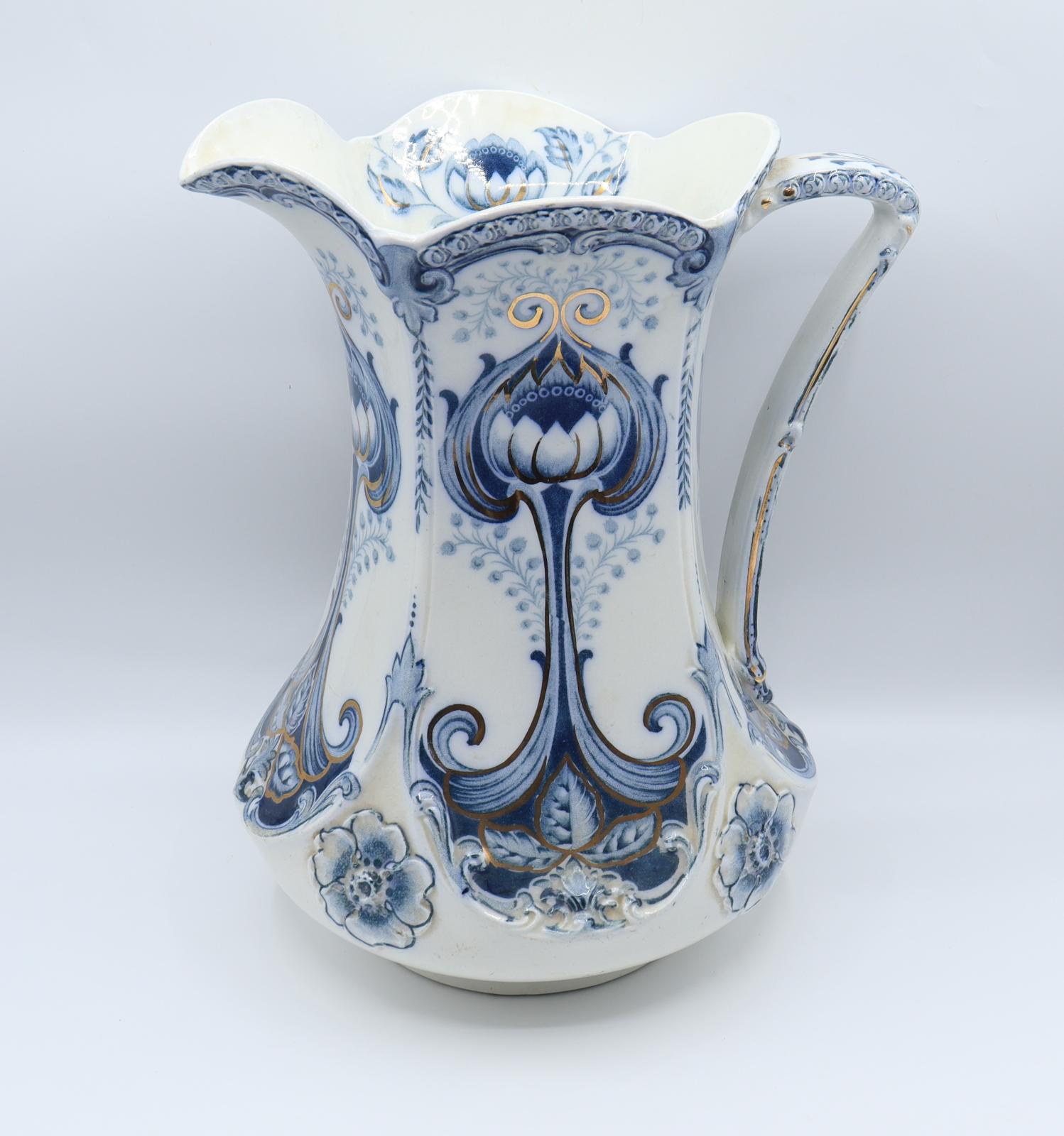 A white, ceramic jug with a bulbous lower body tapering to a narrower neck. The neck is flared with a scalloped rim forming five lobes, two of which form the spout. A single vertical handle runs from the base to be attached under the upper rim. The jug's outside is painted with flower and leaf patterns in blue. There are gilded accents to the blue paintwork. The inside of the jug is white with flowers painted in one spot only. 