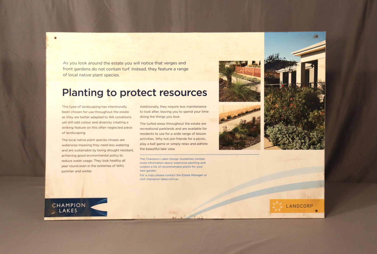A small cream/white, metal sign, displaying navy-blue text and 3 photos referencing "Planting to protect resources".